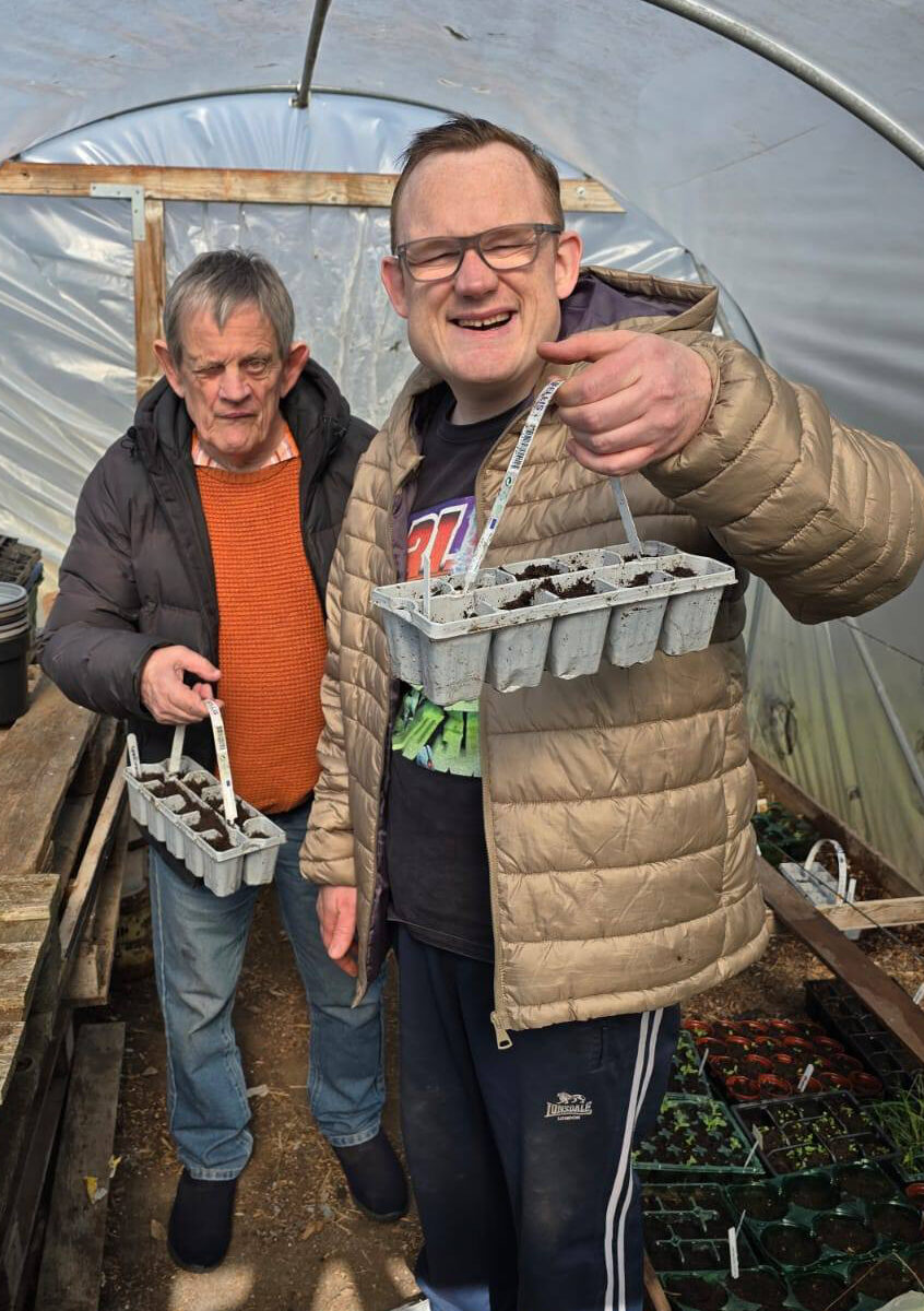 Two men in the poly tunnel holding seedling trays
