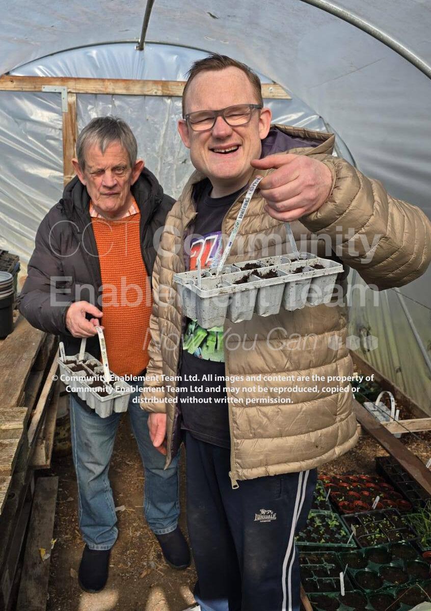 Two men in the poly tunnel holding seedling trays