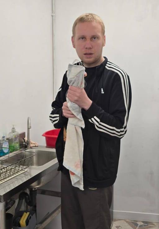 A man standing at a sink, drying dishes with a tea towel during a cooking session.