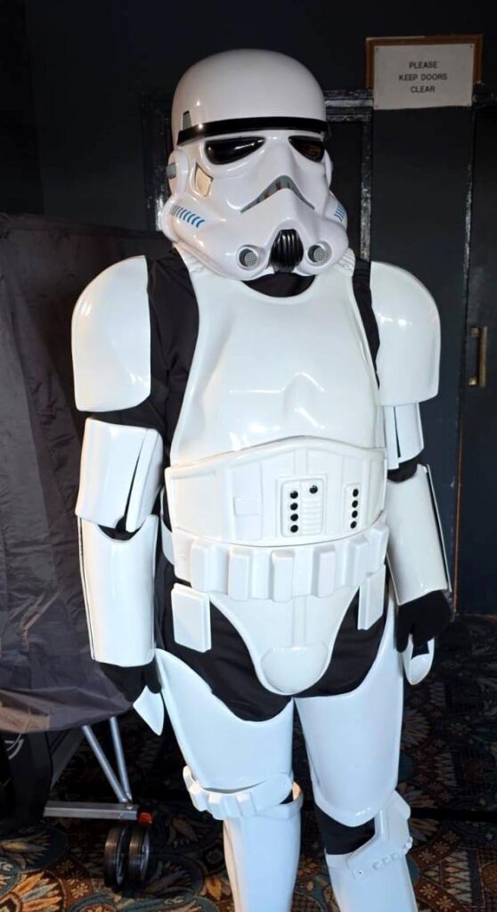 Person dressed in a full Stormtrooper costume standing indoors at the event.