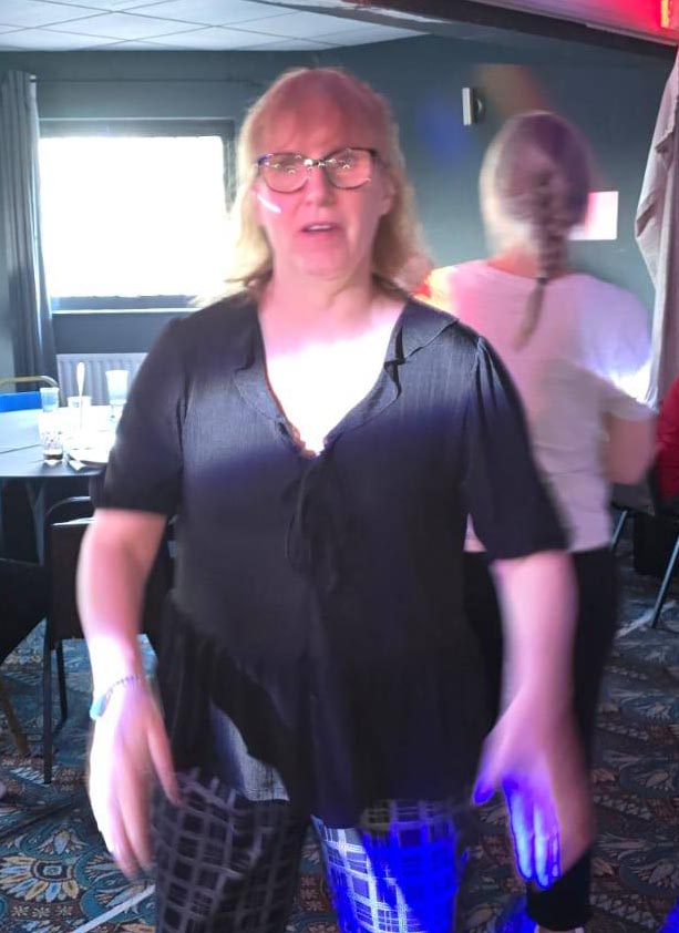 Service user dancing in a dimly lit room with other guests visible in the background.