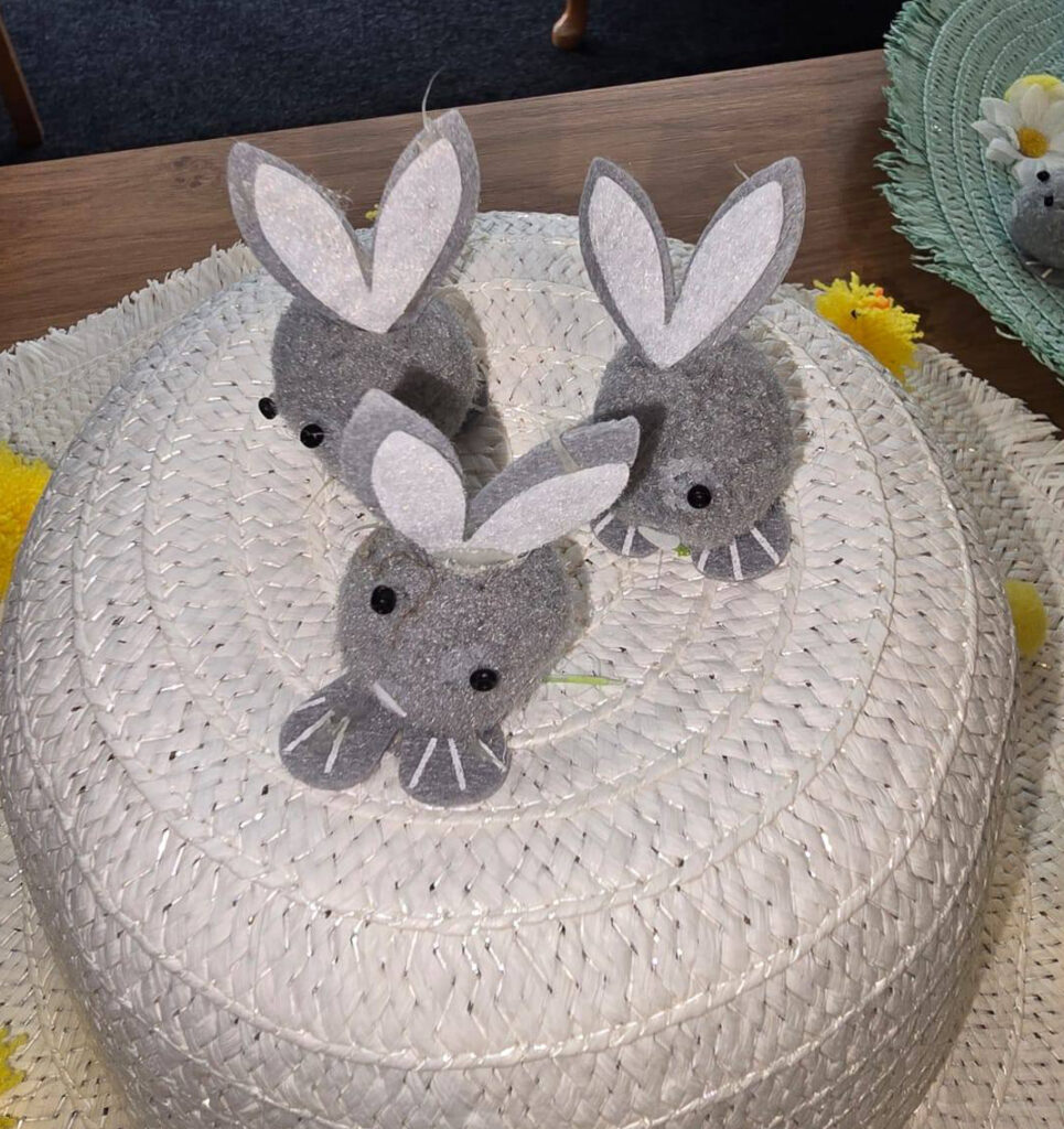 Close-up of a white Easter bonnet decorated with three handmade grey felt bunny faces with ears and button eyes.