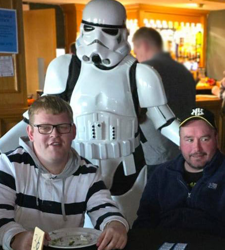 Stormtrooper standing beside a group of friends seated around a table with drinks and snacks at the Easter Disco.