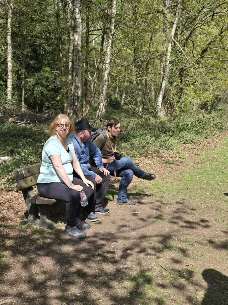 Three members of the group sitting on a bench in the woods, taking a break from their walk.
