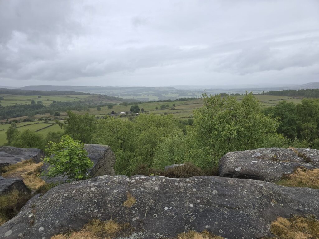A wide view across the Derbyshire countryside from the top of the hill, with fields and trees stretching into the misty distance.