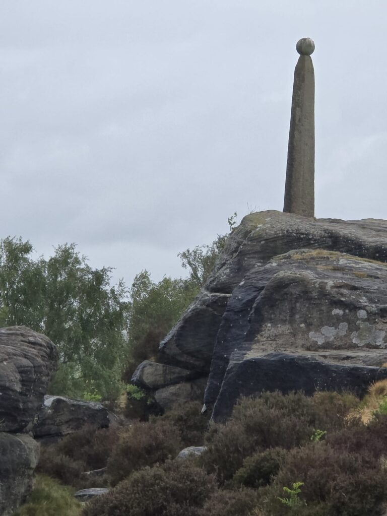 A closer view of the Lord Nelson Monument standing on a rocky platform, surrounded by rugged terrain and heather.
