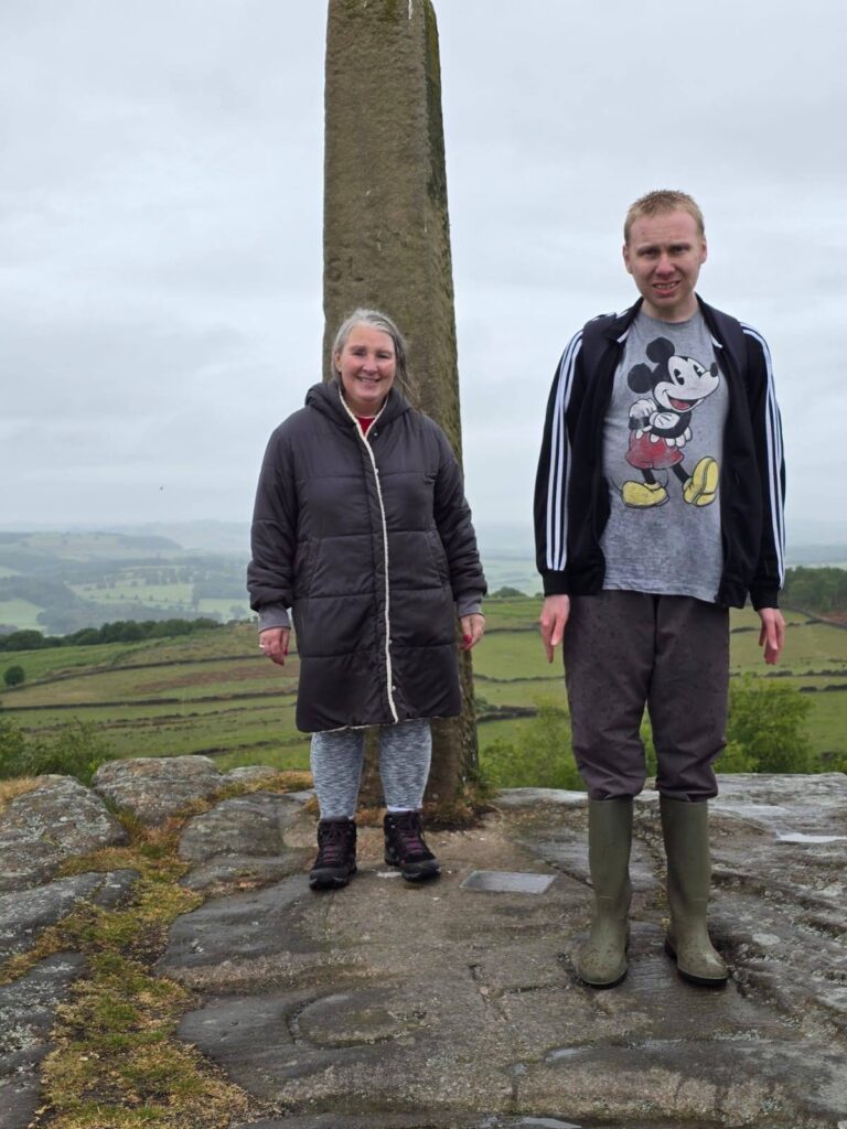Two people, dressed warmly, stand at the base of the Lord Nelson Monument with rolling hills behind them.